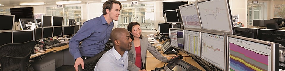 Сотрудники на торговой площадке биржи проверяют данные на большом числе компьютерных экранов